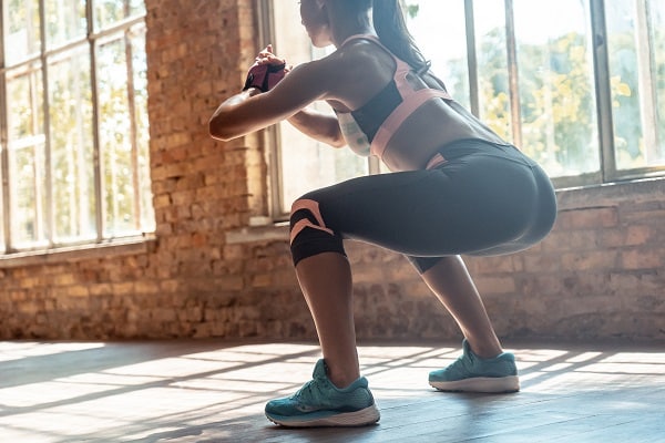 Young fit woman doing squats fitness exercise in gym, rear closeup view